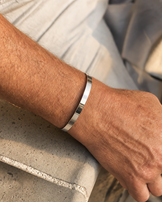 887Seven Meridian Cuff in polished 316L steel, 6mm flat band, worn on a man's wrist resting on a concrete ledge