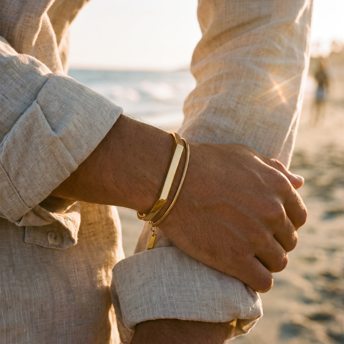 Gold bar bracelet and snake chain worn on a wrist at the beach
