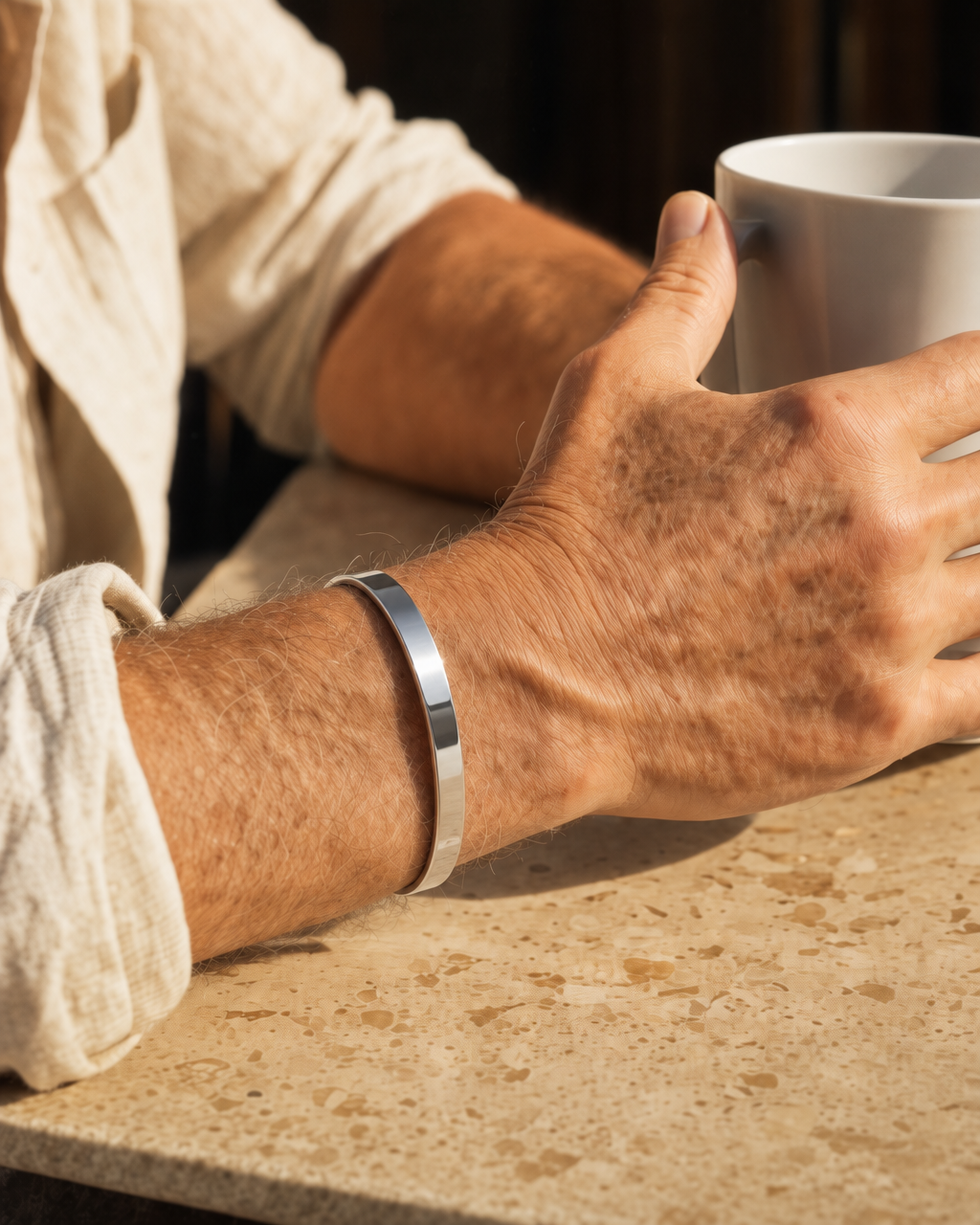 887Seven Meridian Cuff in polished 316L steel, 6mm flat band, worn at a table holding a coffee mug